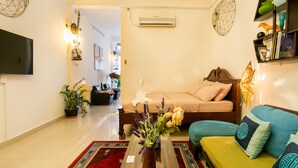 Un salon moderne avec un canapé, une table basse ornée d’un vase, un lit et un téléviseur fixé au mur.