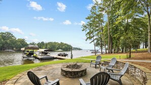 Eine Terrasse im Freien mit Adirondack-Stühlen, einer Feuerstelle und Blick auf einen See mit Booten.