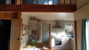 A spacious loft with a high ceiling, wooden beams, a dining area with a table and chairs, a kitchen with modern appliances, and a large window providing natural light. - Cosy spacious Chalet Experience. Beautiful views. (Hanmer Springs)