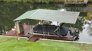 A covered boat dock with a small building, a covered seating area, and a grassy area in front.