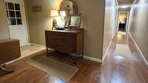 A hallway with wooden flooring, a wooden dresser, a mirror, and a door.