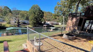A wooden deck with a metal fence, a small pond, and a grassy area with trees in the background.