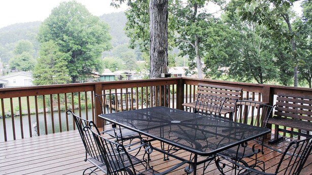 An outdoor deck with a metal table and chairs, surrounded by a wooden railing and trees.
