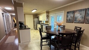 A spacious kitchen with a dining area, featuring a central island, dark wooden chairs, and a tiled floor.