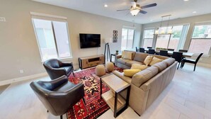 Un salon moderne comprenant un canapé, des fauteuils, un téléviseur et un coin repas avec une table et des chaises.