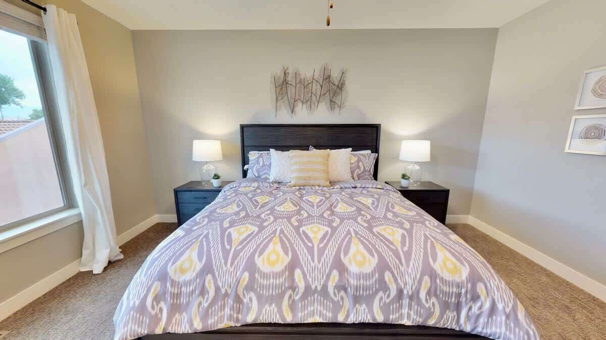 A bedroom with a bed, two bedside tables, a wall-mounted light fixture, and a window with curtains.