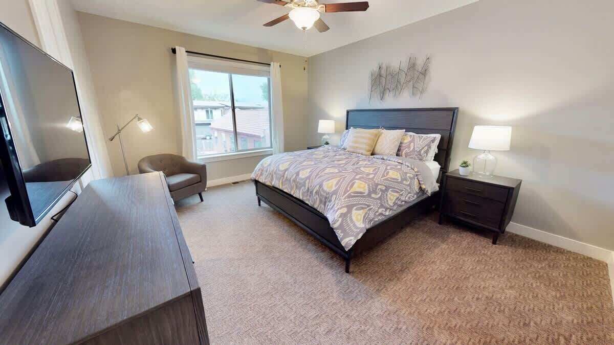 A bedroom with a bed, bedside tables, a desk, a chair, a ceiling fan, and a window.
