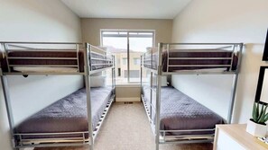 Une chambre avec des lits superposés, une fenêtre et un bureau agrémenté d’une plante.