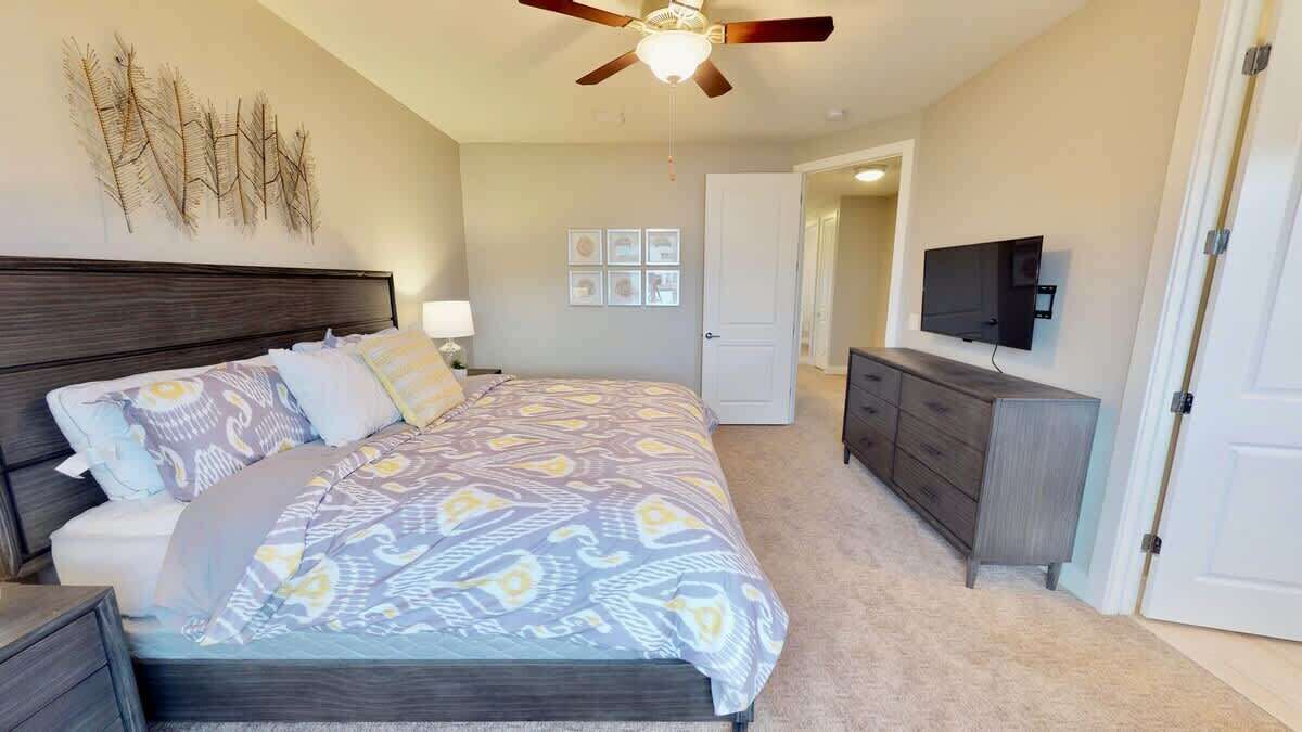 A bedroom with a bed, a dresser, a ceiling fan, and a television.