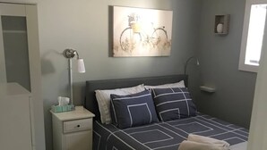Un dormitorio con cama, mesita de noche, lámpara y un cuadro en la pared.