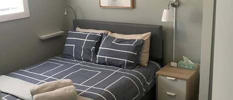 A bedroom with a bed, bedside table, lamp, and a 'FARMHOUSE' sign on the wall.
