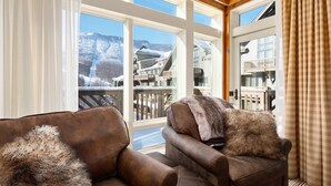 Una sala de estar acogedora con dos sillones de cuero, un ventanal con vistas a una montaña nevada y edificios, y un techo de madera.