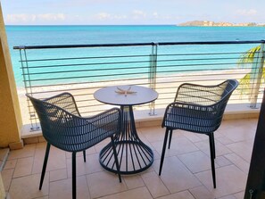 Un balcon avec deux fauteuils en osier noir et une petite table ronde décorée d’une étoile de mer, donnant sur une plage et la mer.