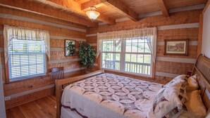 Un dormitorio estilo cabaña acogedor, con una cama grande, paredes de madera y una ventana con vista a una terraza.