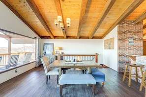 Enjoy meals in this cozy dining area with a large table and comfortable seating, surrounded by a brick fireplace and natural views.