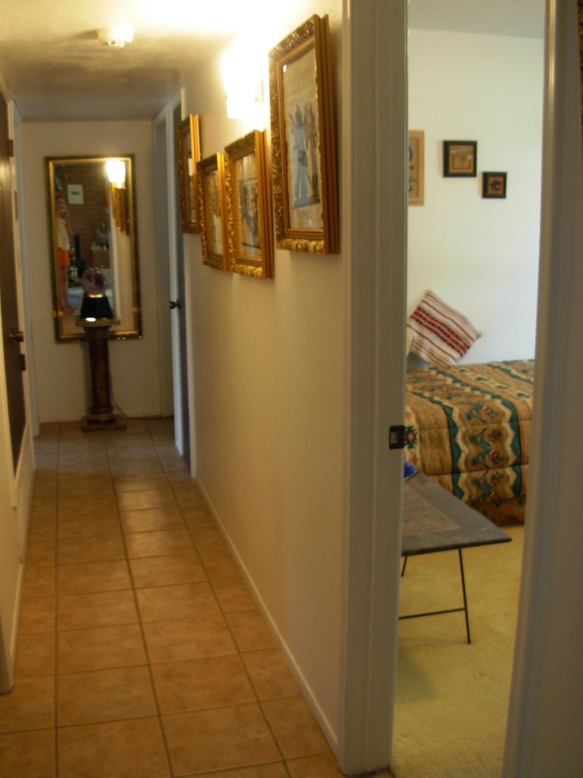 Un pasillo con suelo de baldosas que lleva a un dormitorio con cama y una mesita.