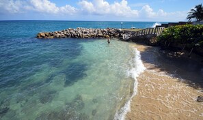 Une plage à l’eau claire, une digue rocheuse et un escalier menant à un point plus élevé.