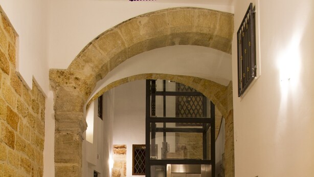 A marble floor with a coat of arms and the words "PALAZZO MOCADA" in a hallway with stone walls and an archway leading to an elevator. - Moncada Houses at Quattro Canti (Palermo)