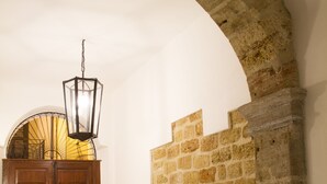 A hallway with a stone wall, a wooden door, and a hanging light fixture. - Moncada Houses at Quattro Canti (Palermo)