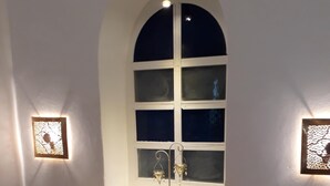 A bedroom with a large arched window, a bed with blue and brown pillows, and two wall-mounted light fixtures.