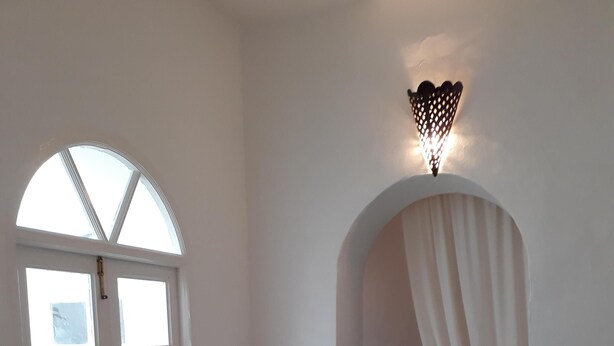 A room with a white door, a blue vase on a small table, a sofa with blue cushions, and a wall-mounted light fixture.