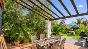 Une terrasse extérieure agrémentée d’une pergola, d’une table avec des chaises, d’un barbecue et d’une végétation luxuriante.