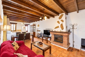 Ein gemütliches Wohnzimmer mit Kamin, Holzbalken, einer Couch und einem Fernseher.