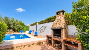 Un jardin avec une piscine, un barbecue en pierre et un espace détente avec des chaises.