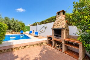 A backyard with a swimming pool, a stone barbecue grill, and a seating area with chairs. - Cubo's Casa La Viña / private pool / air conditioning / free wifi (Alhaurín el Grande)