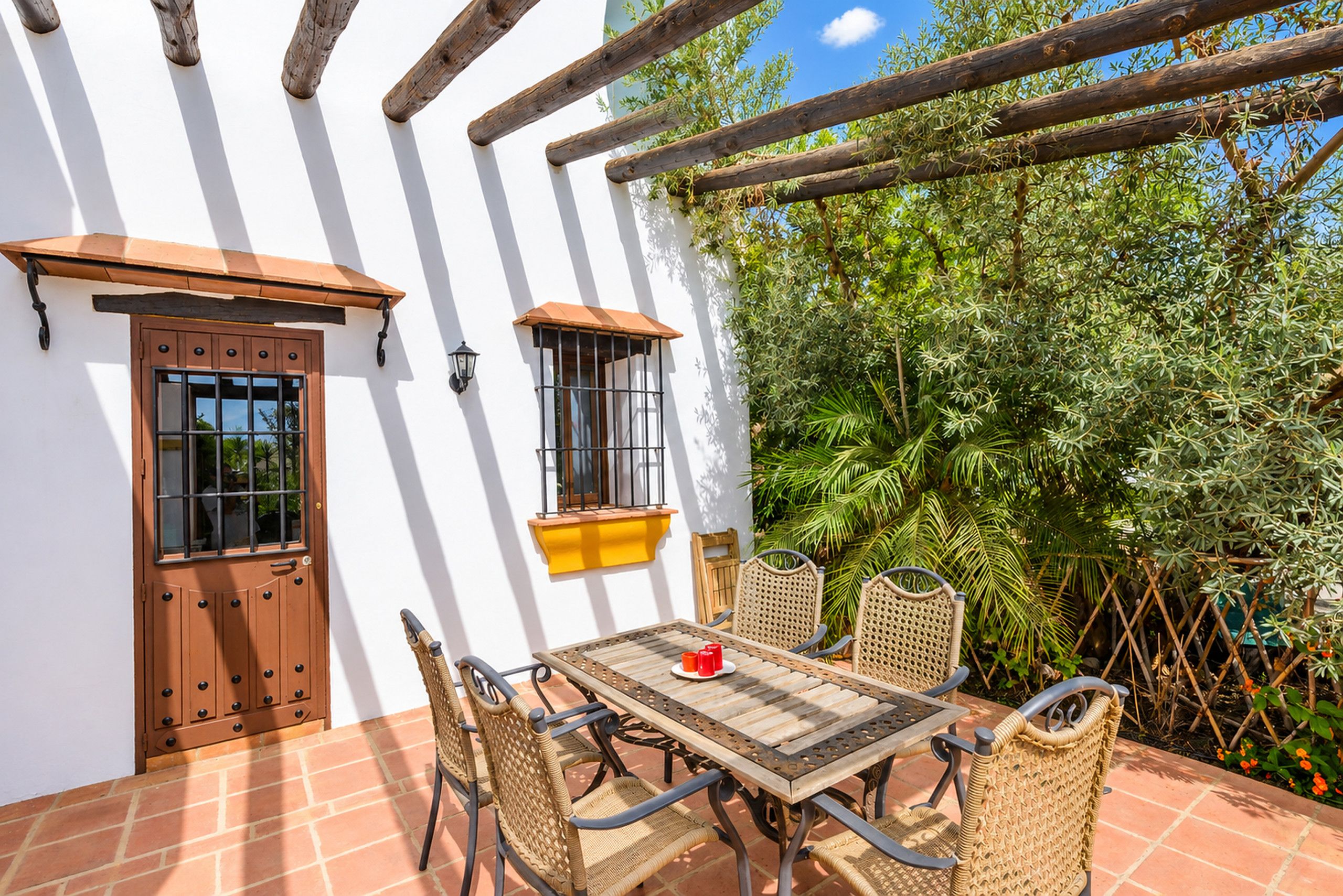 A patio with a table and chairs, a wooden door, and a window with a metal grill.