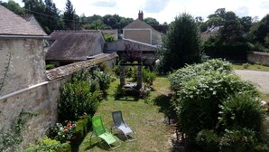 Ein Innenhof mit zwei grünen Stühlen, einer Steinsäule und einem Garten mit verschiedenen Pflanzen und Blumen.
