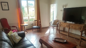 Ein Wohnzimmer mit einer Ledersofa, einem Holztisch und einem Fernseher auf einem Holzschrank.