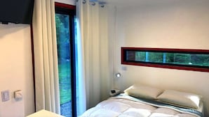 Un dormitorio con una cama, una ventana con cortinas, una mesita de noche y un televisor montado en la pared.