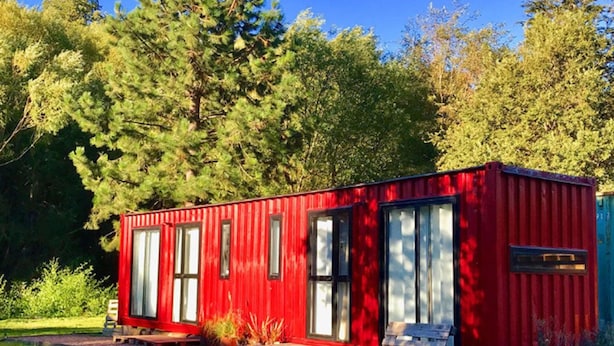 Una casa contenedor roja con ventanas grandes, un banco de madera y un sendero de grava.