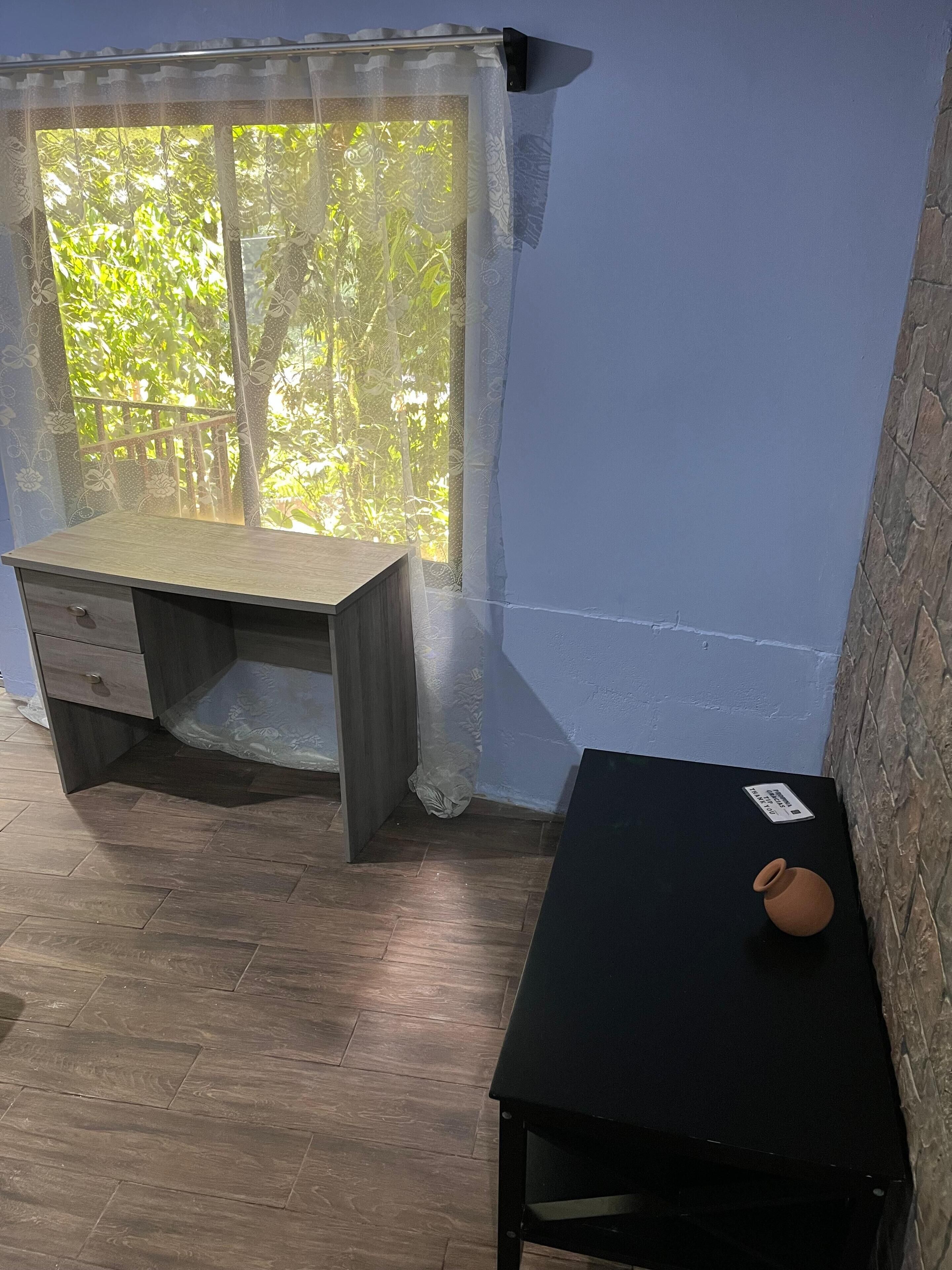 Een kamer met een houten bureau, een zwarte tafel en een raam met kantgordijnen.