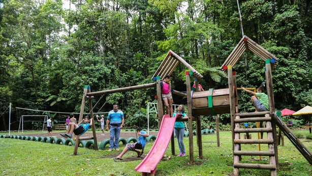 A playground with a wooden climbing structure, a slide, and a swing set. - Recreo Verde Hot Springs & Spa (Venecia)