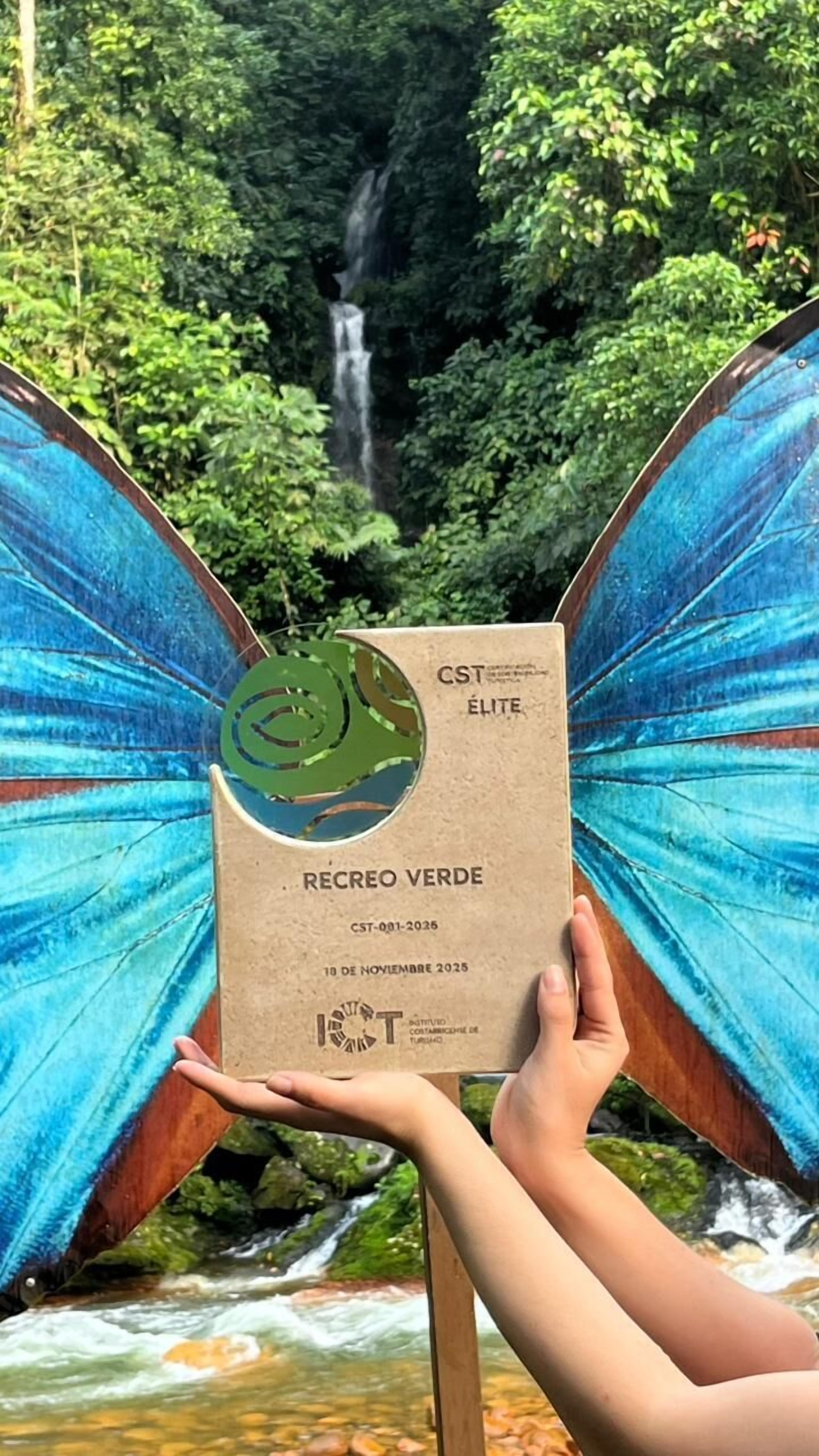 Eine Person hält eine CST ELITE Karte mit grünem Logo vor dem Hintergrund eines Wasserfalls und üppiger Vegetation.