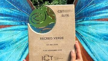 Eine Person hält eine CST ELITE Karte mit grünem Logo vor dem Hintergrund eines Wasserfalls und üppiger Vegetation.