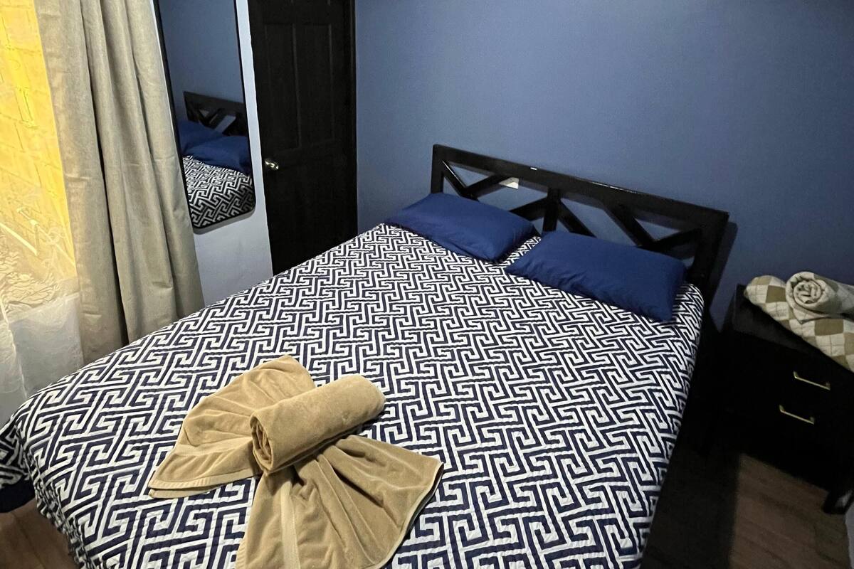 A bedroom with a bed, a nightstand, a mirror, and a painting on the wall.
