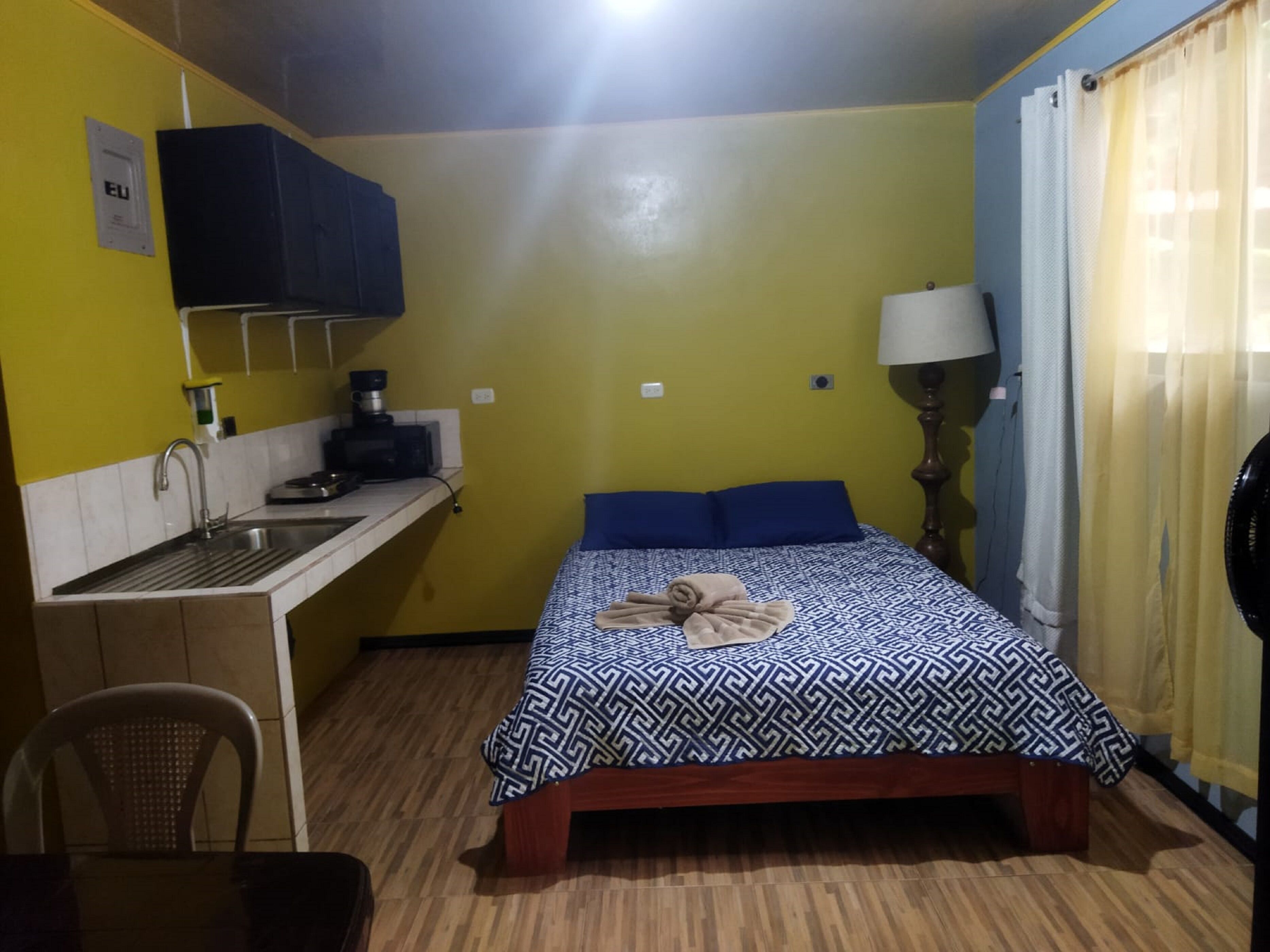 A compact room with a bed, a small desk with a sink, a chair, and a lamp.