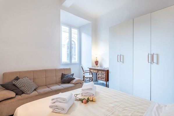 A bedroom with a bed, a sofa, a desk, and a wardrobe.