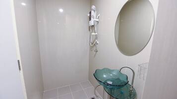 A bathroom with a glass sink, a handheld showerhead, and a wall-mounted mirror.