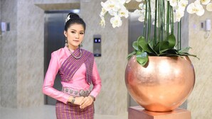 A person standing next to a large copper pot with white orchids. - Wish Hotel Ubon (Ubon Ratchathani)