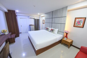 Un dormitorio moderno con una cama grande, un escritorio de madera, una silla roja y una mesita de noche con un florero.