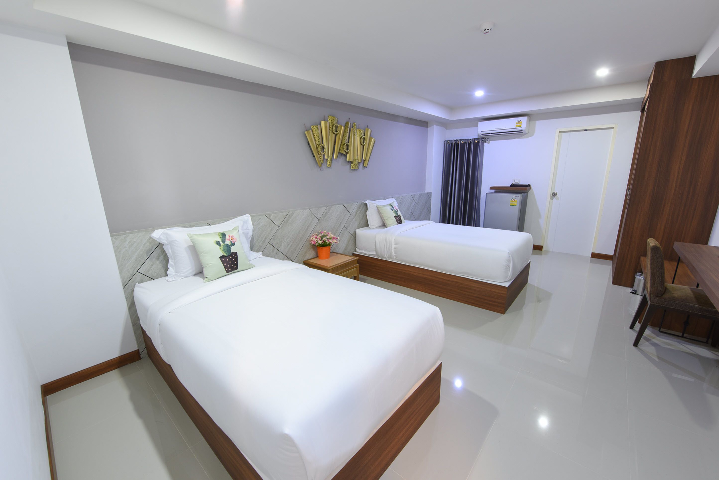 A hotel room with two beds, a wooden nightstand, a small table, and a desk.