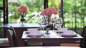 A dining table set with white plates, bowls, and wine glasses, with pink flowers in the background. - Wish Hotel Ubon (Ubon Ratchathani)