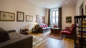 A living room with a sofa, armchairs, a coffee table, a bookshelf, and framed pictures on the wall.