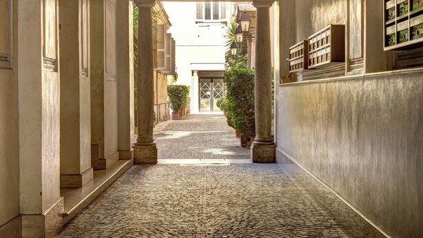 A cobblestone alleyway with classical architecture, including columns and a covered entrance.
