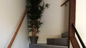 Un escalier aux marches grises et à la rampe en bois, menant à un palier où se trouve un pot de fleurs.