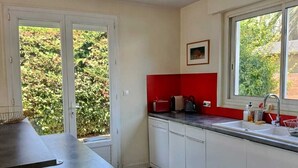 Une cuisine moderne avec des meubles blancs, un plan de travail noir, un pare-feu rouge et une grande fenêtre.